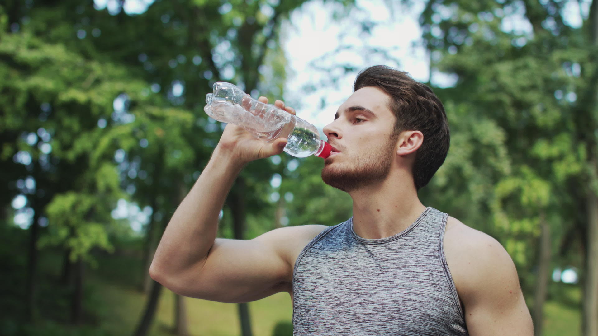 夏季公园运动后运动男子从瓶子里喝水视频的预览图