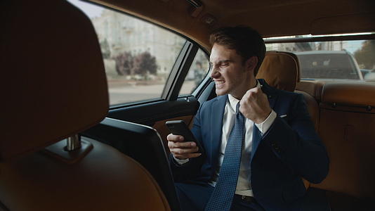 职业男性在现代汽车中使用智能手机并获得好消息视频的预览图