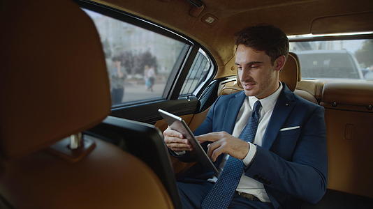 汽车里的职业男性在平板电脑上收到好消息微笑着视频的预览图