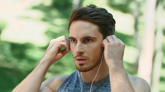 运动男子在公园早上用耳机听音乐视频的预览图