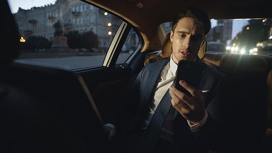 商人在黑暗的豪华轿车中通过视频电话发言视频的预览图