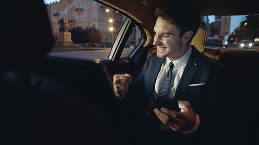 职业男性在豪华车上看到电话里的好消息欣喜若狂视频的预览图