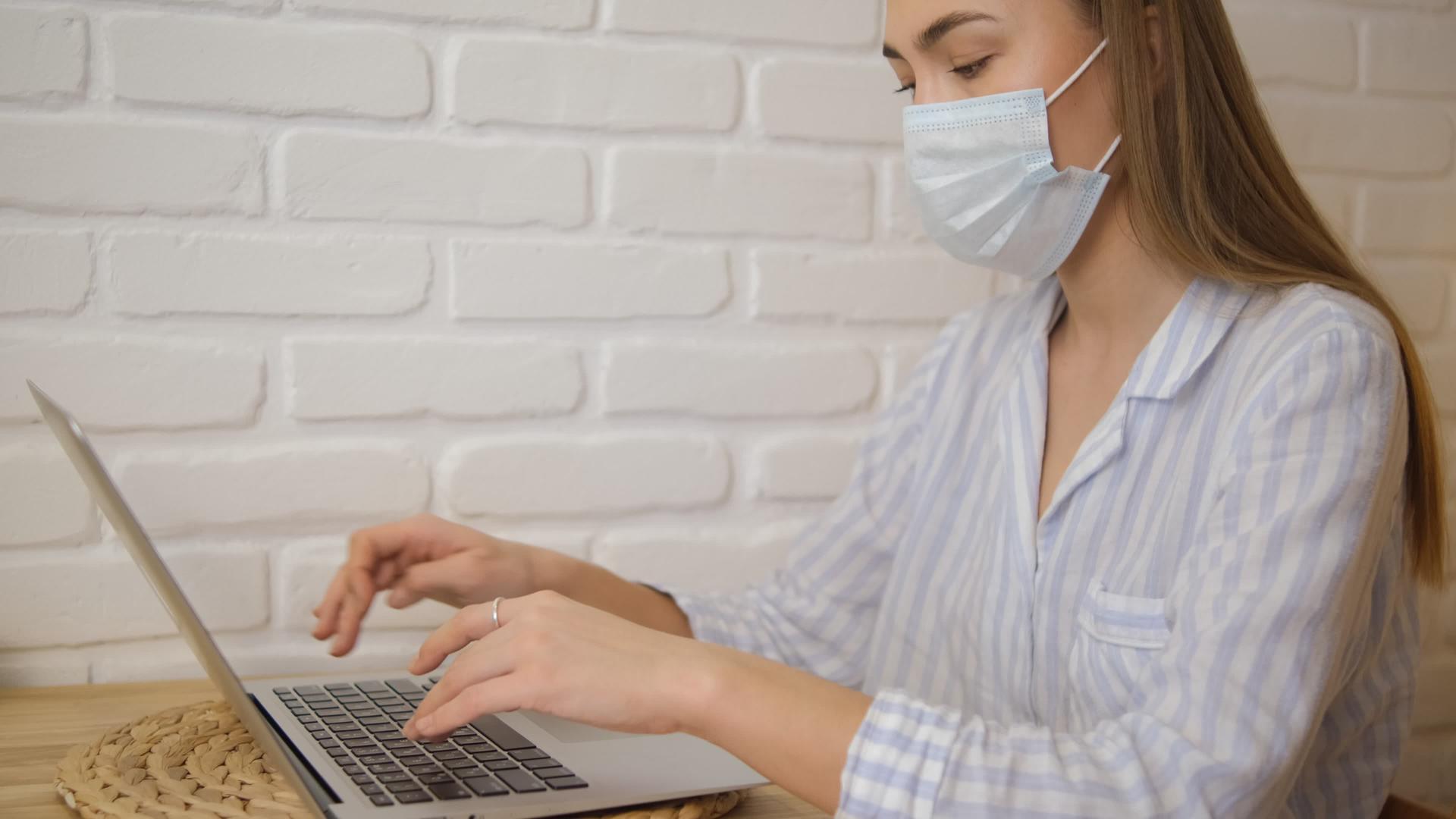 一个戴着医用口罩和条纹睡衣的女孩在家工作视频的预览图