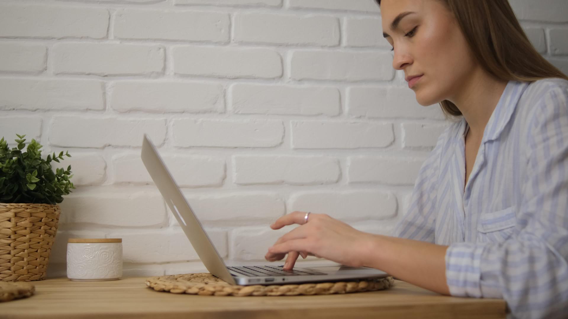 一个穿着条纹睡衣的女孩在家远程工作在电脑后面笔记本电脑键入文本打印选择性焦点视频的预览图