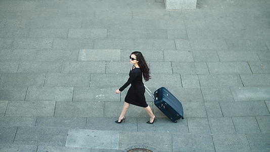 时尚的黑色连衣裙女性在街上拉着行李箱出差视频的预览图