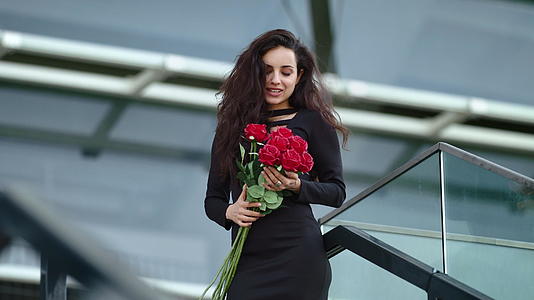 特写女人在街上捧着红玫瑰闻着花香微笑着视频的预览图