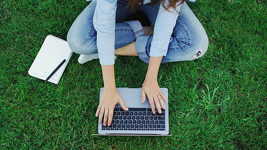 顶级女性在公园绿草上工作时会在笔记本键盘上打字视频的预览图