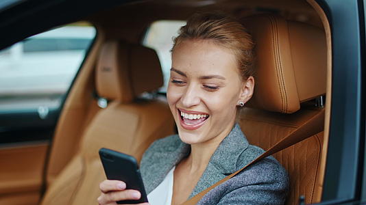 白领女性在驾驶座上看手机微笑面部特写视频的预览图