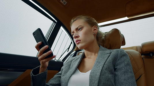 白领女性坐在汽车后座在智能手机上读坏消息皱着眉头视频的预览图