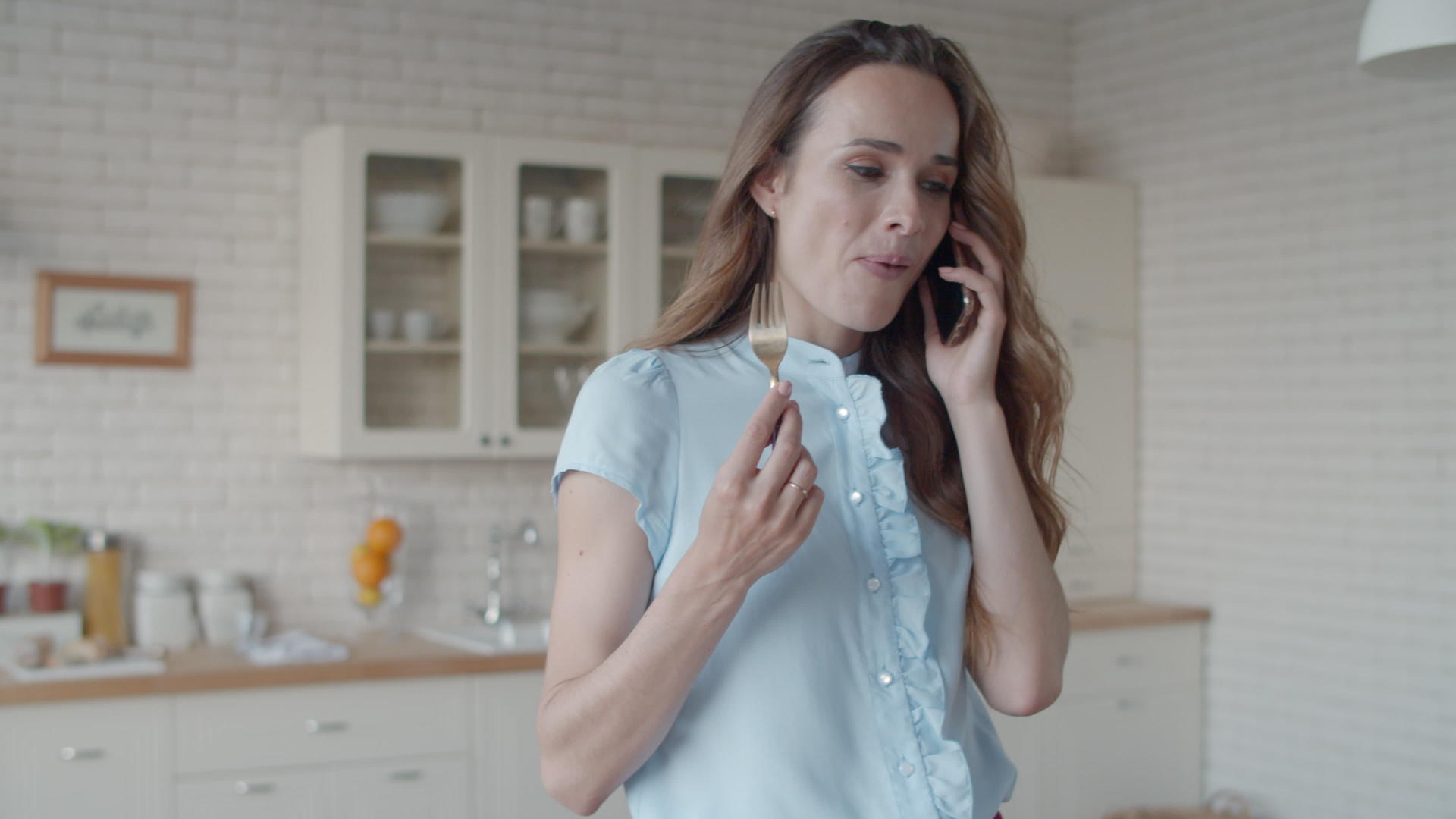 年轻女性在白色厨房谈论手机视频的预览图
