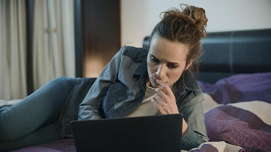 年轻女性用膝盖电脑躺在家庭沙发上视频的预览图