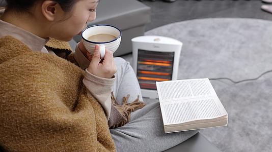 坐在沙发上取暖喝咖啡看书的女生视频的预览图