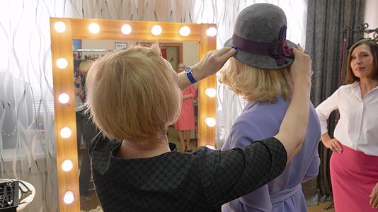 优雅的女性在时尚精品店前镜中选择时尚帽视频的预览图