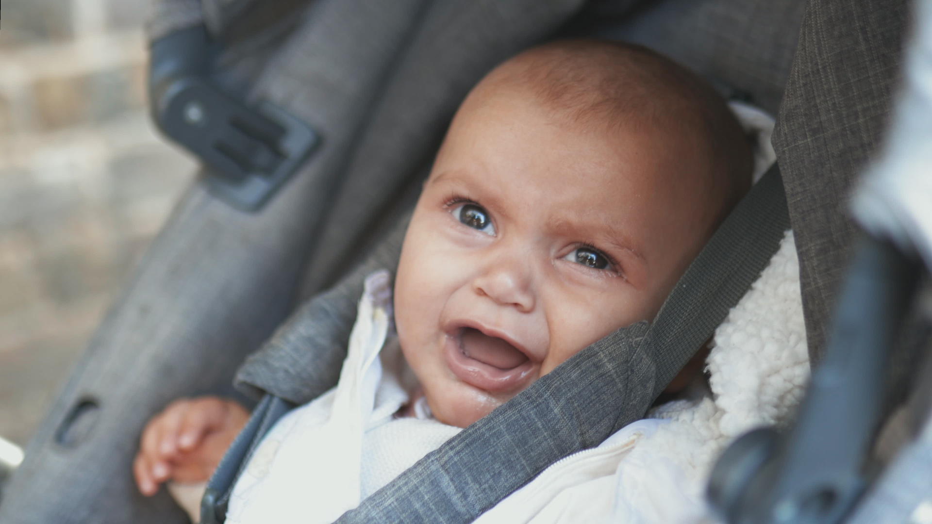 在一辆灰色婴儿车里哭泣的婴儿悲伤地看着相机视频的预览图