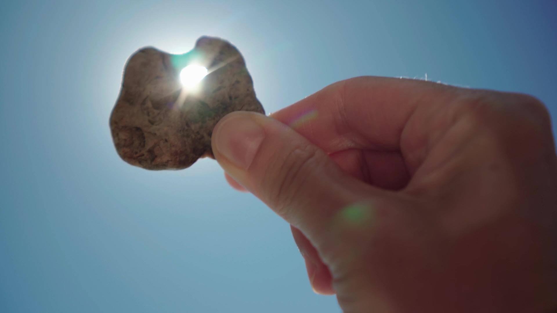 手里拿着一块有洞的小石头面对着太阳视频的预览图