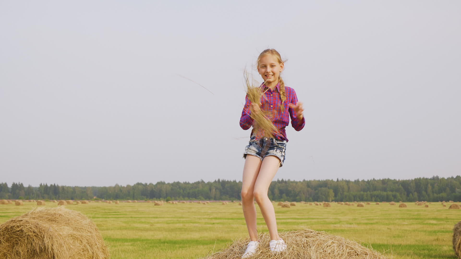 这个淘气的女孩在收割田里手里拿着稻草在干草堆上跳舞视频的预览图