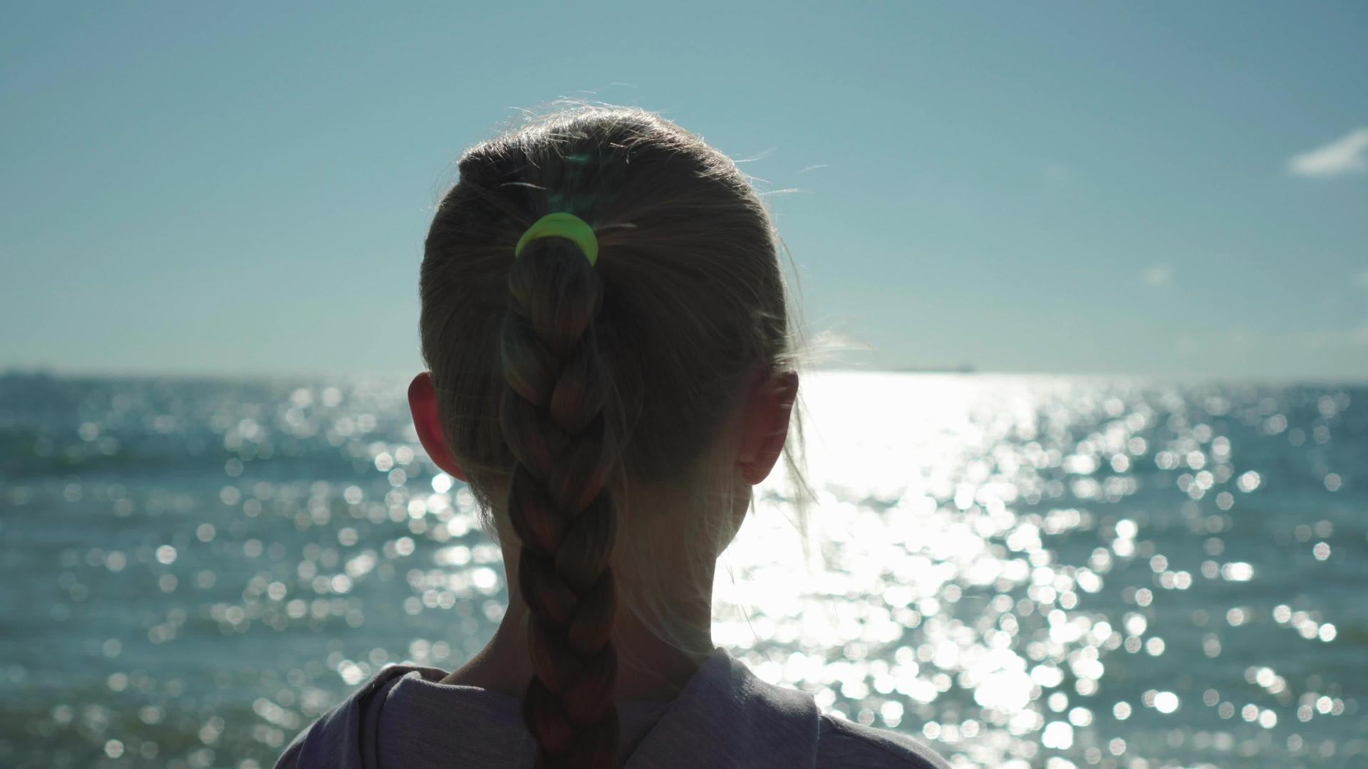 看看金发小女孩特写的日落和闪闪发光的海水视频的预览图
