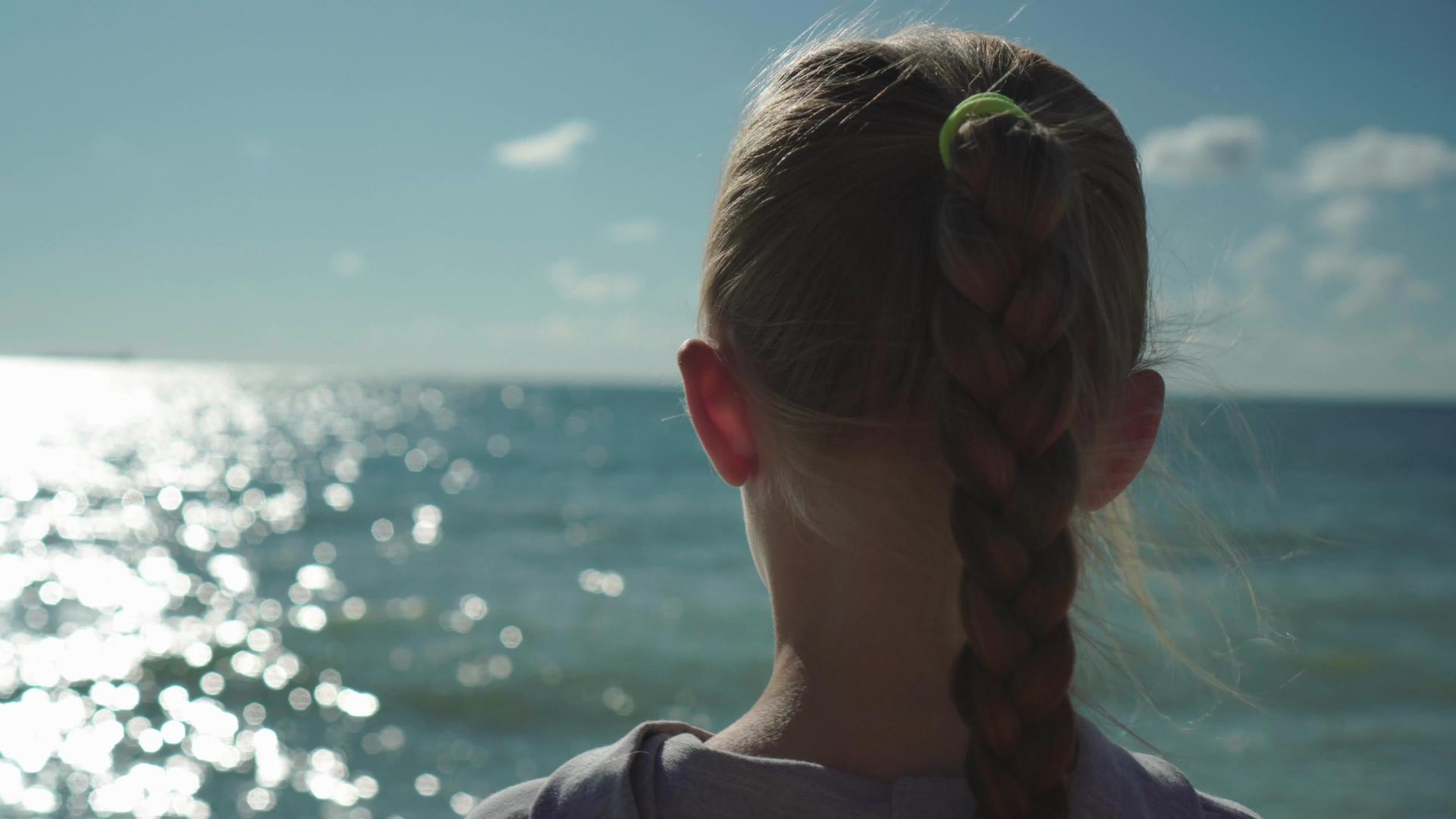 看看金发小女孩特写的日落和闪闪发光的海水视频的预览图