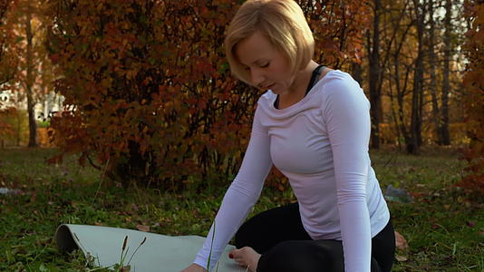 秋季公园户外运动时健身女性在地毯上伸展身体视频的预览图