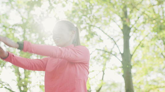 健康的女孩在公园里伸展手臂和脖子在跑步前加热运动视频的预览图
