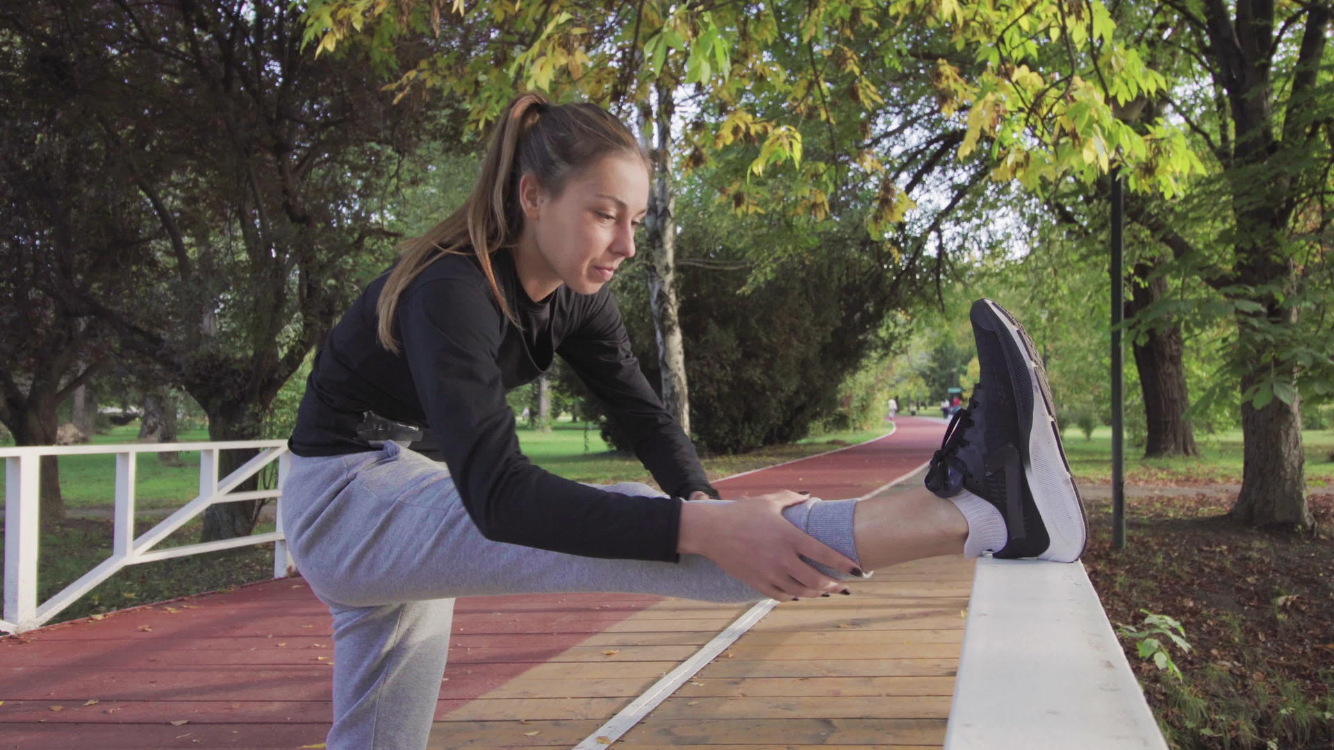 女孩在木桥栅栏上伸展双腿以加热跑步运动视频的预览图
