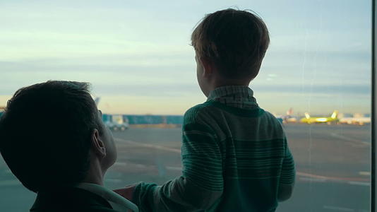 儿子和父亲透过窗户看着机场地区视频的预览图