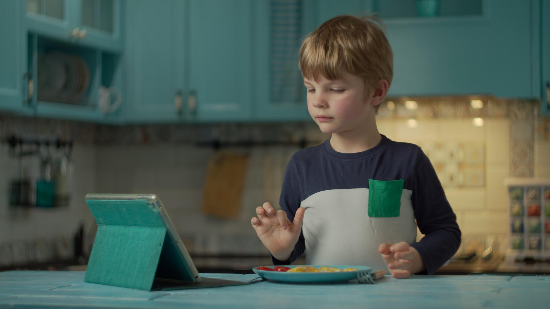 小男孩吃西红柿炒鸡蛋在家看平板电脑视频的预览图