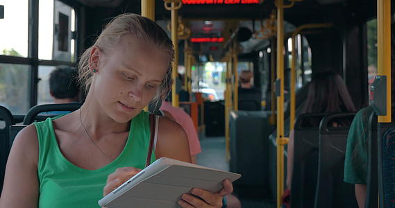 年轻女性乘坐公共汽车时使用坐垫娱乐视频的预览图