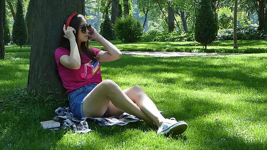 年轻女孩在美丽的公园里听音乐视频的预览图