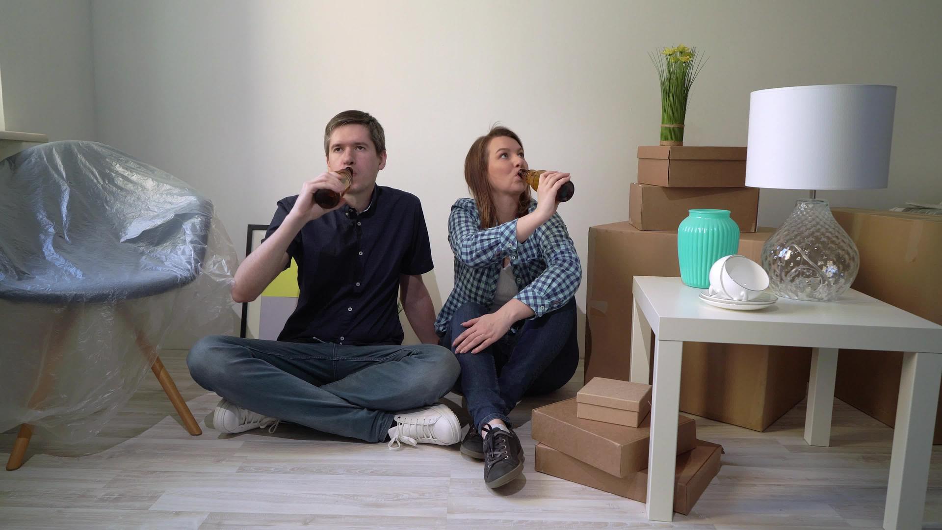 一对年轻夫妇坐在一楼在公寓里休息喝啤酒视频的预览图