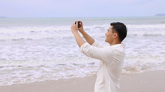 海边使用手机拍照的男青年视频的预览图
