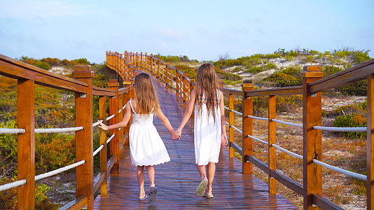 可爱的小女孩在去白色热带海滩的路上在木桥上视频的预览图