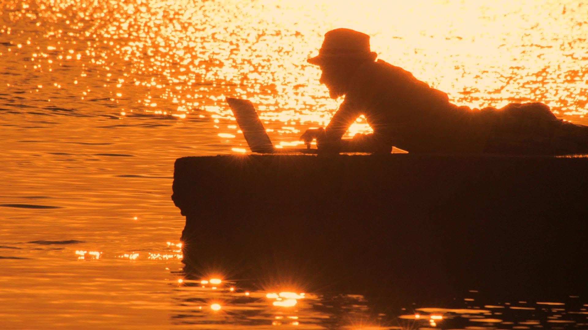 男人躺在码头上用笔记本电脑剪影视频的预览图