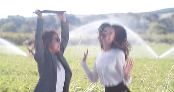 两名拥有笔记本电脑的女性商人在田野里跳跃和庆祝成功视频的预览图