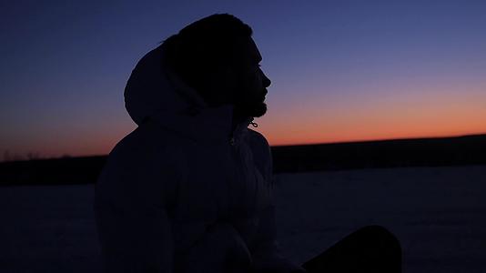 一个戴着兜帽的年轻人坐在夕阳下视频的预览图