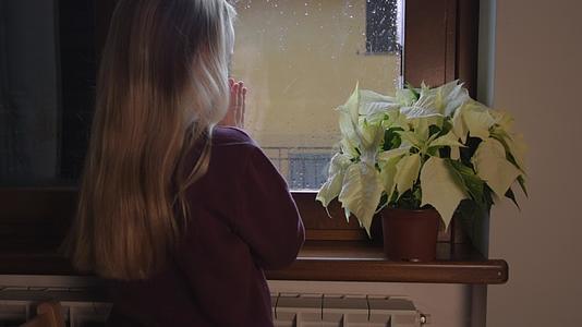 金发女孩站在窗前用呼吸温暖她的手视频的预览图