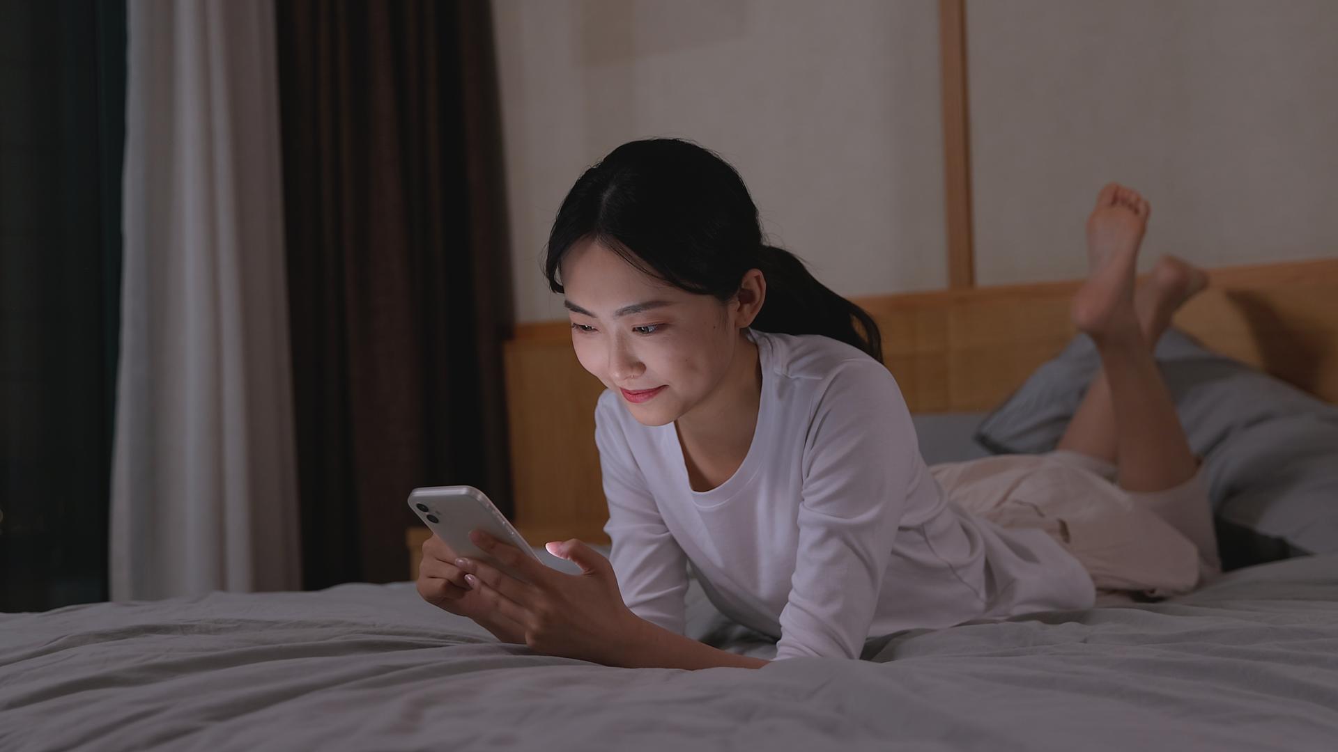 女孩卧室床上轻松玩手机聊天视频的预览图