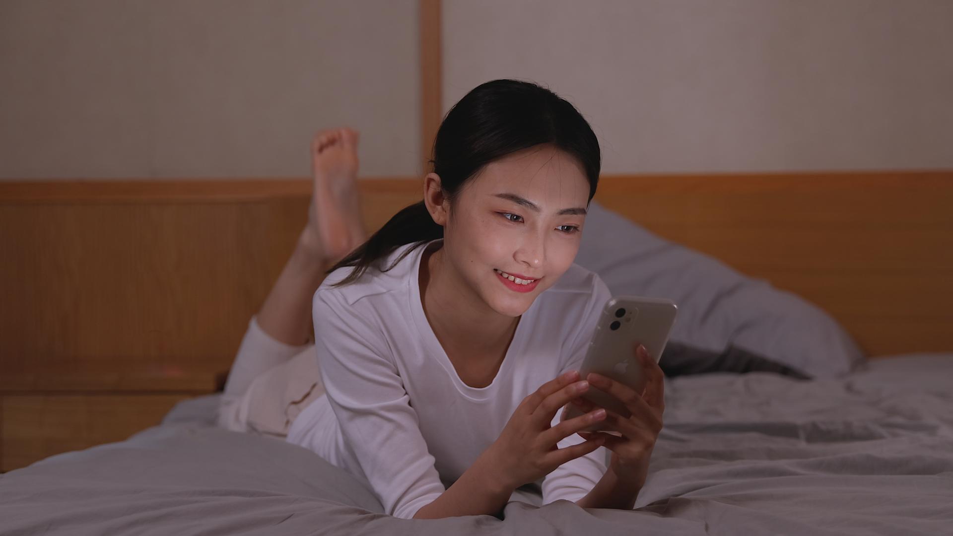 女孩卧室床上轻松玩手机聊天视频的预览图