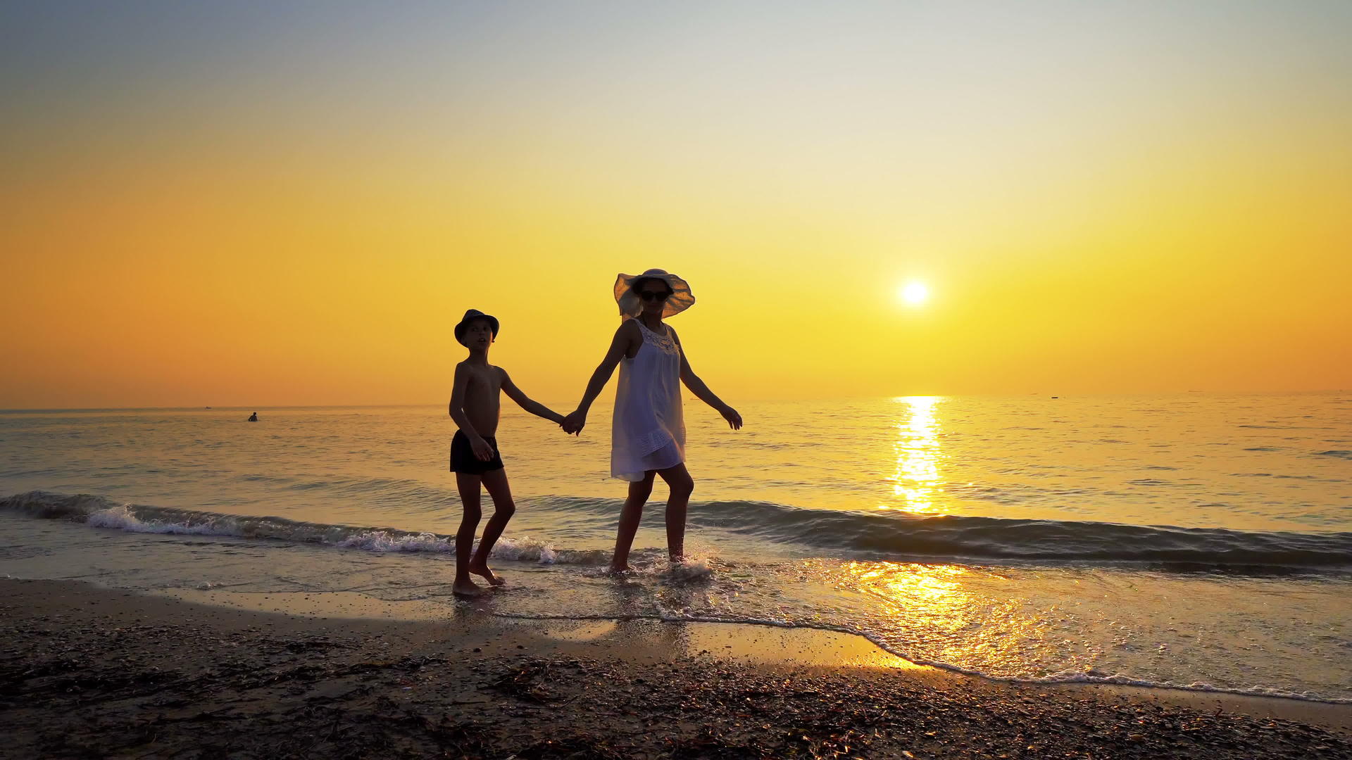 母亲和儿子日落时在海滩上散步视频的预览图