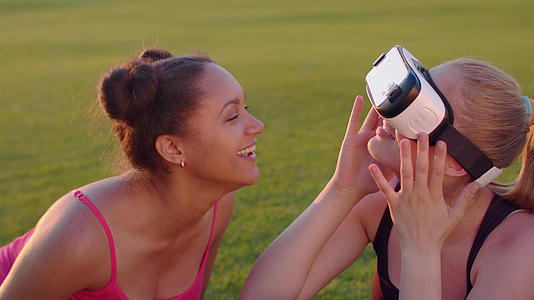 坐在草坪上体验两位年轻女性的体验vr眼镜视频的预览图