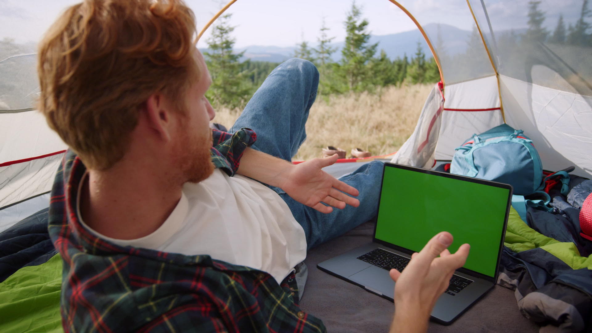 山顶露营在帐篷里男人躺在旁边用笔记本电脑聊天开会视频的预览图