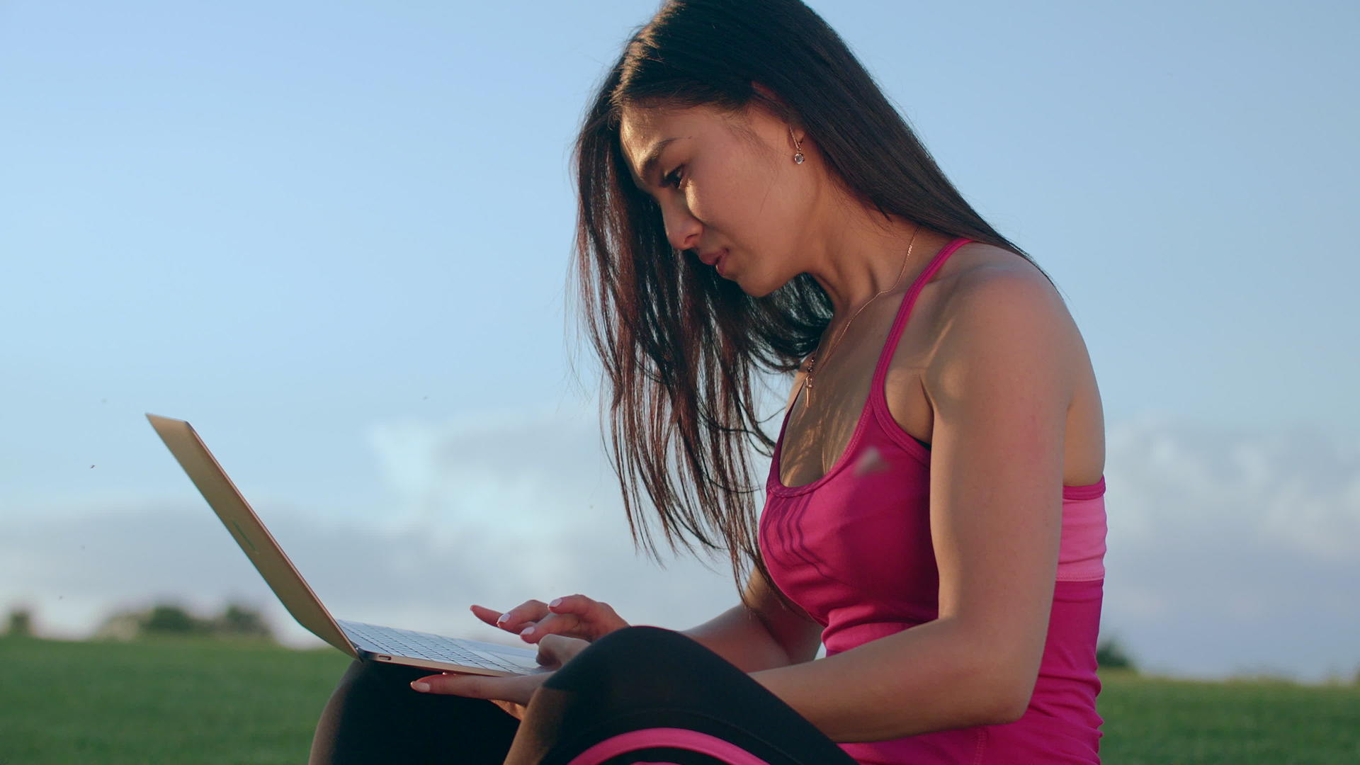 年轻女性坐在公园的草地上看着笔记本电脑视频的预览图