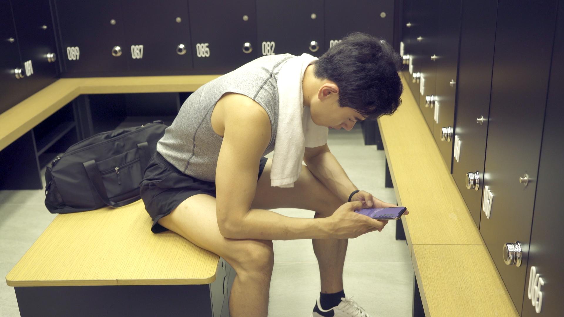 更衣室里的男青年坐着使用手机视频的预览图