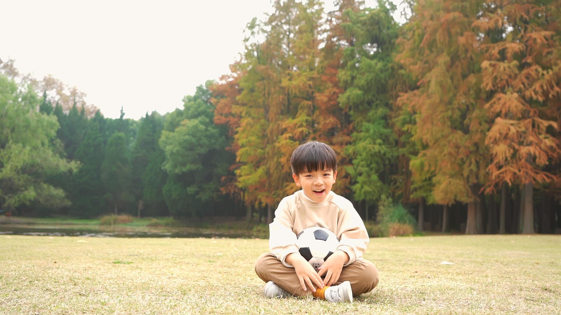 秋天坐在公园草地上的小男孩抱着足球视频的预览图