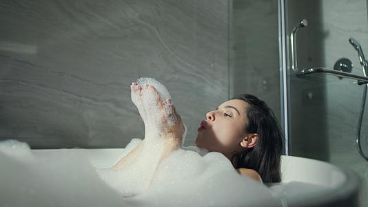 微笑的女孩在浴室的浴缸里吹泡泡视频的预览图