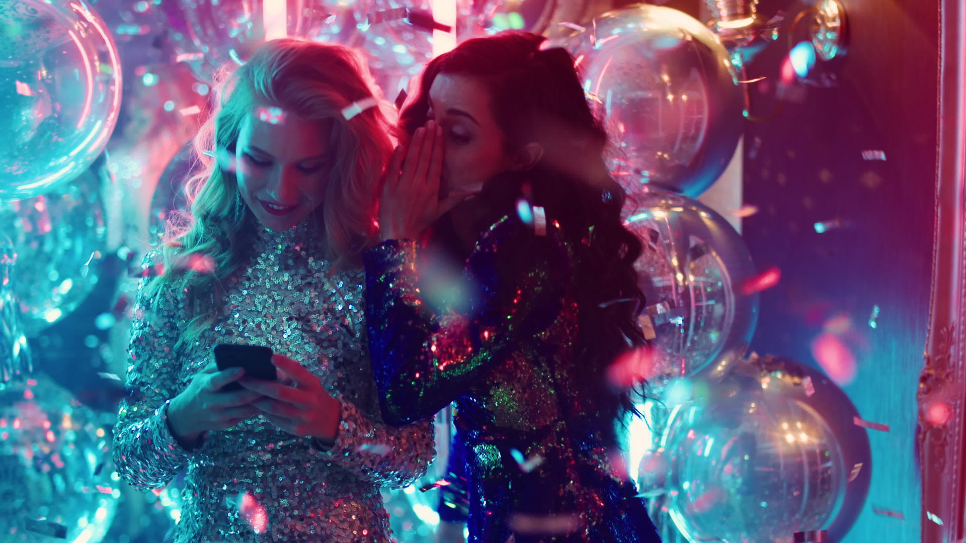 两个女孩在酒吧夜店一边说悄悄话一边看手机视频的预览图