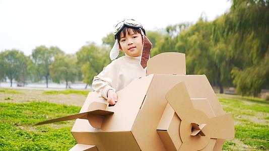 秋季公园草地上玩纸盒飞机的小男孩升格视频视频的预览图