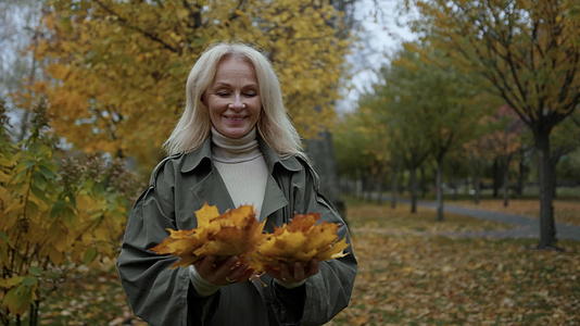 在秋天的公园里慢动作和叶子玩得开心的老妇人视频的预览图