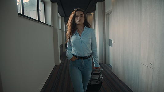美丽的女人正在寻找酒店房间里有决心的女孩拉着行李箱走廊视频的预览图