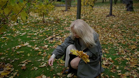一位穿灰色大衣美丽的老太太在公园里收集树叶视频的预览图